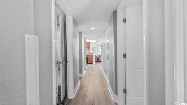 hallway featuring light wood-style flooring, baseboards, and a textured wall