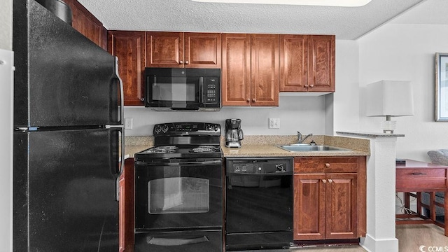 kitchen featuring black appliances, a textured ceiling, brown cabinets, and a sink