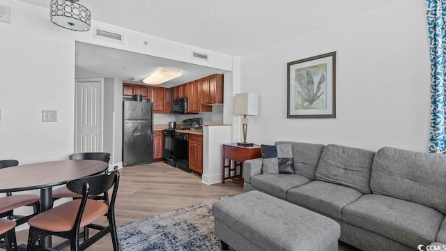 living room featuring visible vents, light wood-style flooring, and a textured ceiling