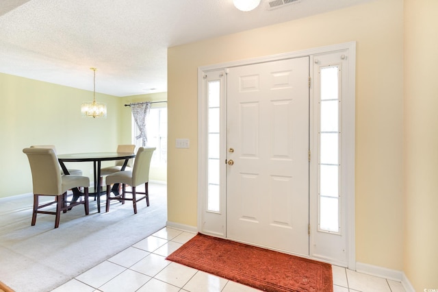 foyer entrance featuring a textured ceiling, an inviting chandelier, and light tile patterned floors