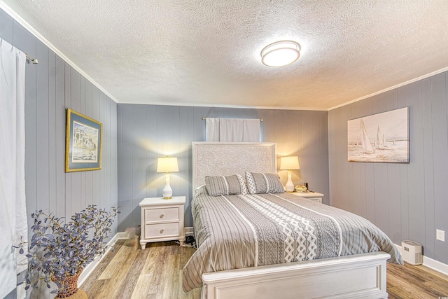 bedroom featuring baseboards, a textured ceiling, ornamental molding, and wood finished floors