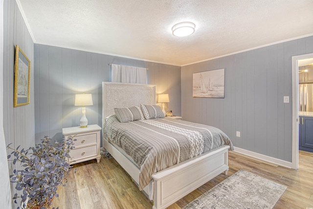 bedroom featuring crown molding, light wood-style flooring, a textured ceiling, stainless steel fridge, and baseboards