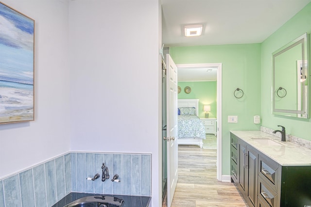 ensuite bathroom with a tub to relax in, ensuite bathroom, wood finished floors, and vanity