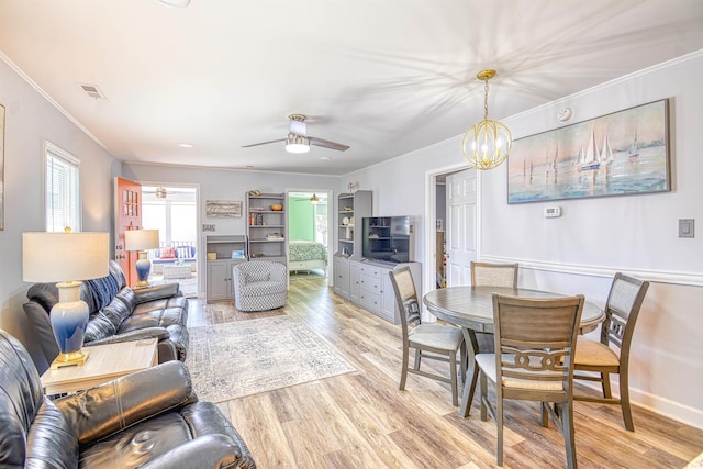 living area with ceiling fan with notable chandelier, ornamental molding, light wood-type flooring, and visible vents