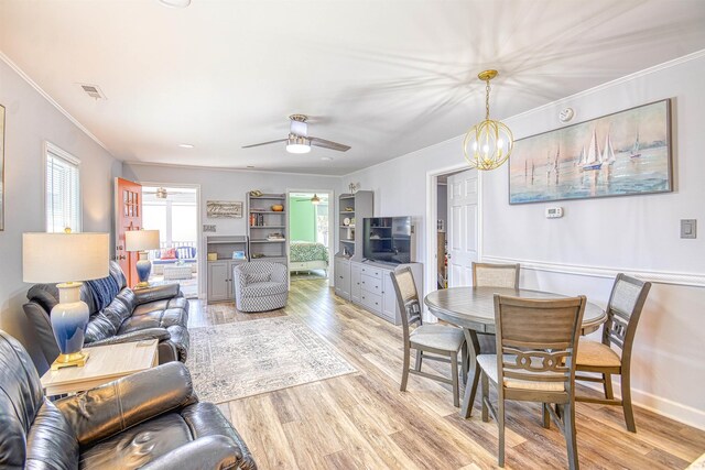 dining room featuring crown molding, visible vents, light wood finished floors, and ceiling fan with notable chandelier