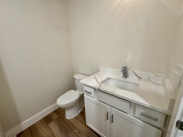 half bath featuring vanity, baseboards, wood finished floors, and toilet