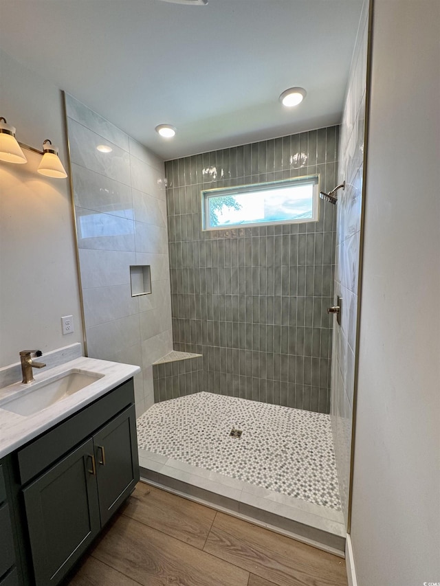 bathroom with a tile shower, wood finished floors, and vanity
