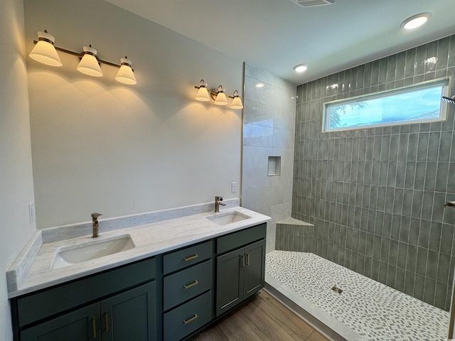 full bath featuring double vanity, a walk in shower, a sink, and wood finished floors