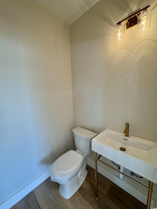 half bath featuring baseboards, toilet, and wood finished floors