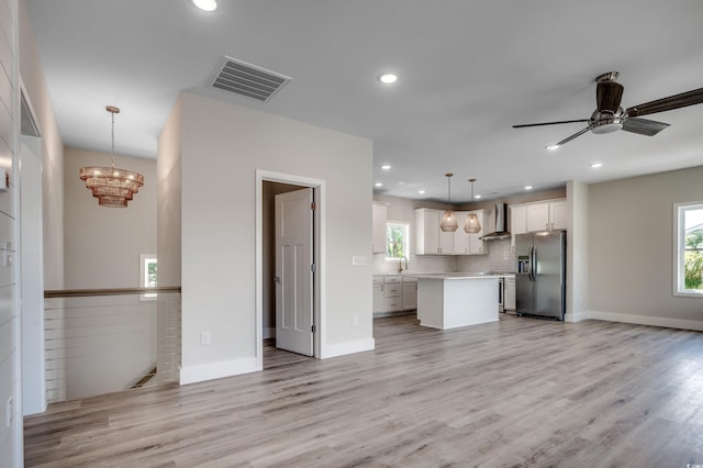 kitchen featuring stainless steel refrigerator with ice dispenser, pendant lighting, a kitchen island, wall chimney exhaust hood, and white cabinets