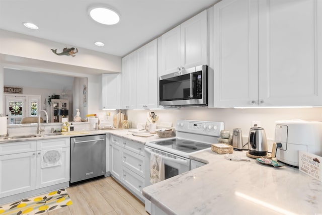 kitchen featuring white cabinetry, appliances with stainless steel finishes, light stone counters, and a sink