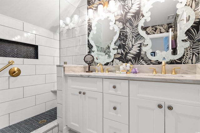 full bathroom with double vanity, visible vents, a tile shower, and a sink