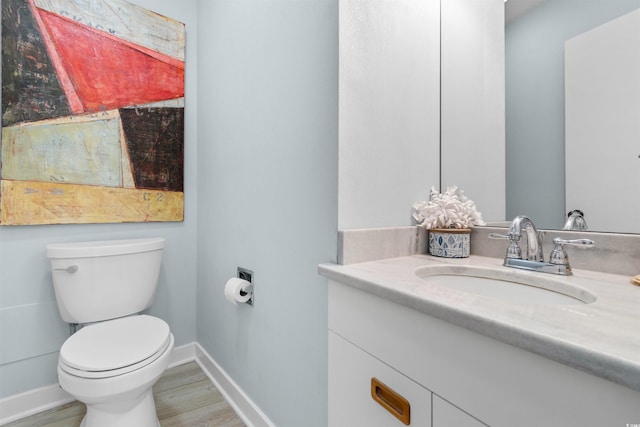 half bath with vanity, wood finished floors, toilet, and baseboards