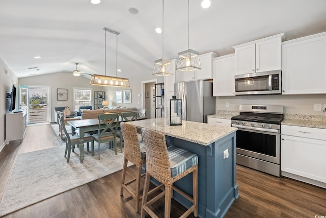 kitchen with appliances with stainless steel finishes, open floor plan, decorative light fixtures, a center island, and white cabinetry