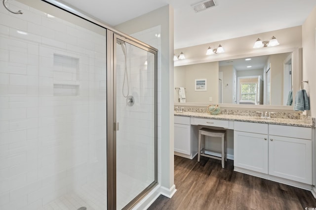 full bath with a stall shower, double vanity, visible vents, and wood finished floors