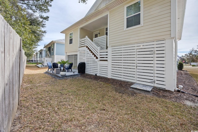 view of side of property with a patio, stairway, a lawn, and fence