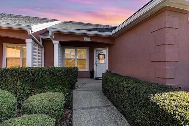 property entrance featuring a shingled roof and stucco siding