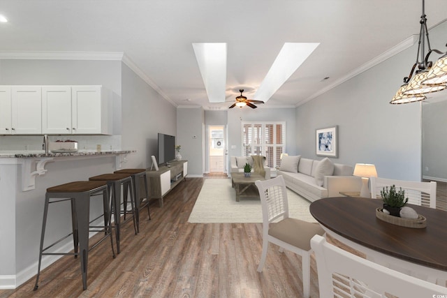 living room with a skylight, baseboards, ceiling fan, dark wood-type flooring, and crown molding