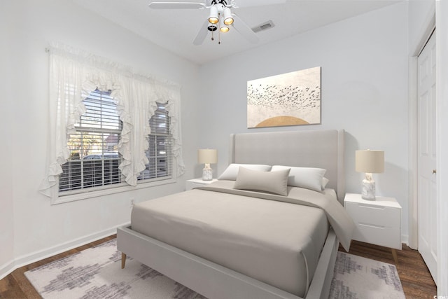 bedroom with baseboards, visible vents, dark wood finished floors, ceiling fan, and a closet