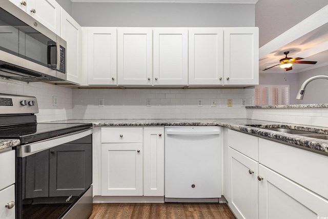 kitchen with stainless steel appliances, a sink, white cabinets, decorative backsplash, and dark stone counters