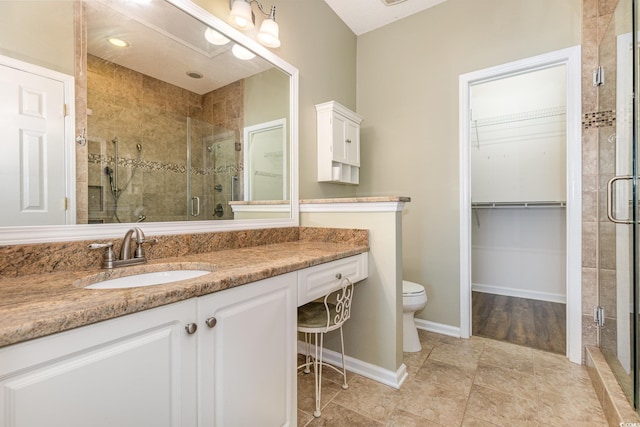 bathroom featuring a walk in closet, toilet, a stall shower, vanity, and baseboards