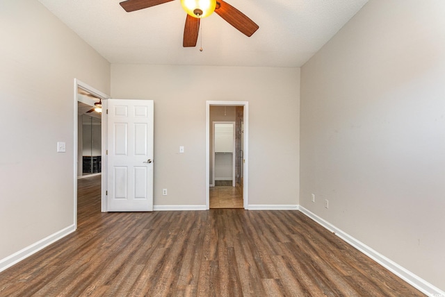 unfurnished bedroom with ceiling fan, a spacious closet, dark wood-style flooring, and baseboards