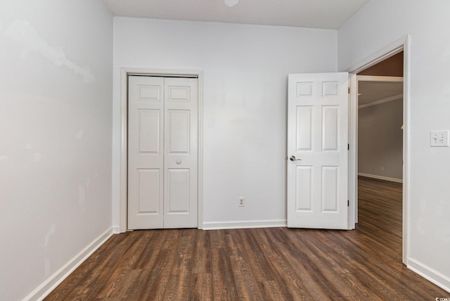 unfurnished bedroom featuring dark wood-type flooring, a closet, and baseboards