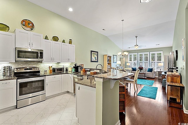 kitchen with dark stone counters, decorative backsplash, a peninsula, a kitchen breakfast bar, and stainless steel appliances