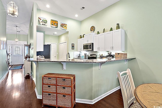 kitchen featuring a breakfast bar, a peninsula, dark wood finished floors, stone countertops, and stainless steel appliances