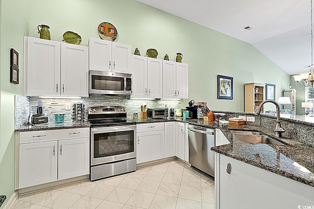 kitchen with a sink, dark stone countertops, stainless steel appliances, a chandelier, and vaulted ceiling