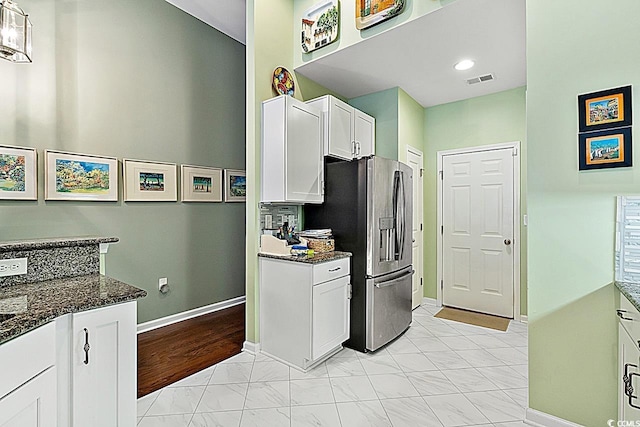 kitchen with visible vents, stainless steel refrigerator with ice dispenser, dark stone counters, white cabinets, and baseboards