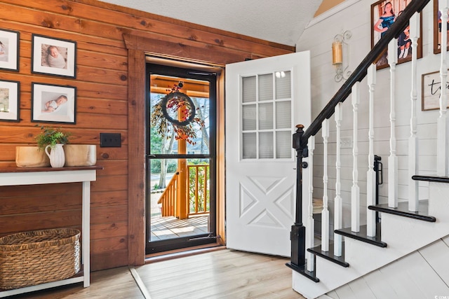 interior space featuring light hardwood / wood-style flooring, wood walls, a textured ceiling, and lofted ceiling