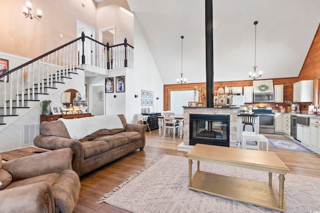 living room with high vaulted ceiling, light hardwood / wood-style floors, an inviting chandelier, and a wood stove