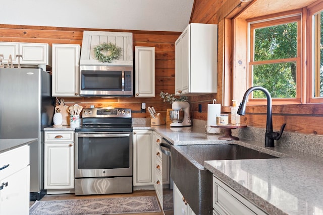 kitchen with sink, stainless steel appliances, white cabinetry, and wood walls