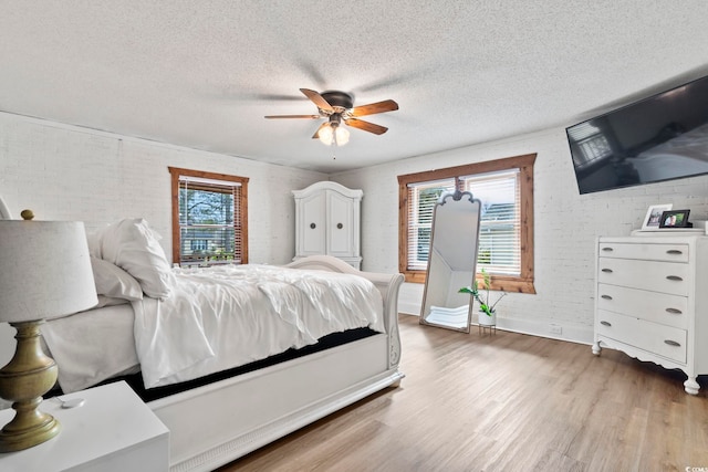 bedroom with a textured ceiling, ceiling fan, brick wall, and wood-type flooring