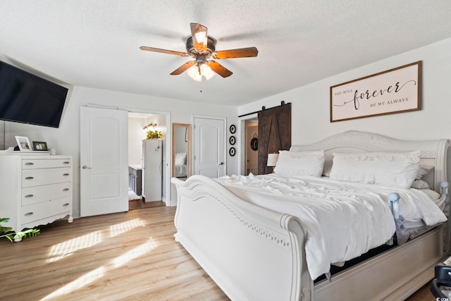 bedroom with light hardwood / wood-style flooring, ceiling fan, a barn door, and a textured ceiling