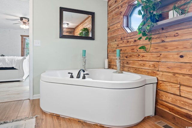 bathroom with ceiling fan, a tub to relax in, and hardwood / wood-style floors