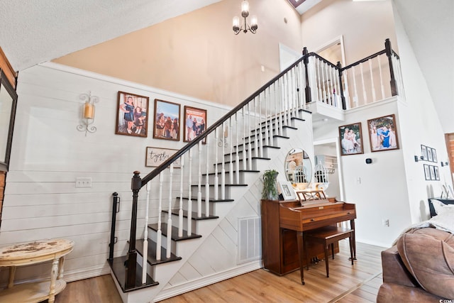 staircase with a high ceiling, a textured ceiling, hardwood / wood-style floors, and an inviting chandelier