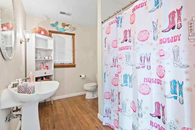 bathroom with hardwood / wood-style flooring, a shower with curtain, toilet, and a textured ceiling