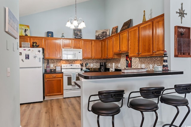 kitchen featuring dark countertops, white appliances, decorative light fixtures, and a kitchen bar