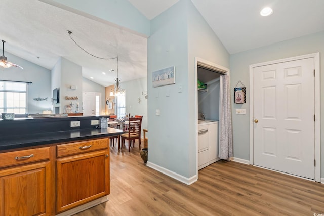 kitchen featuring pendant lighting, light wood finished floors, dark countertops, brown cabinetry, and vaulted ceiling