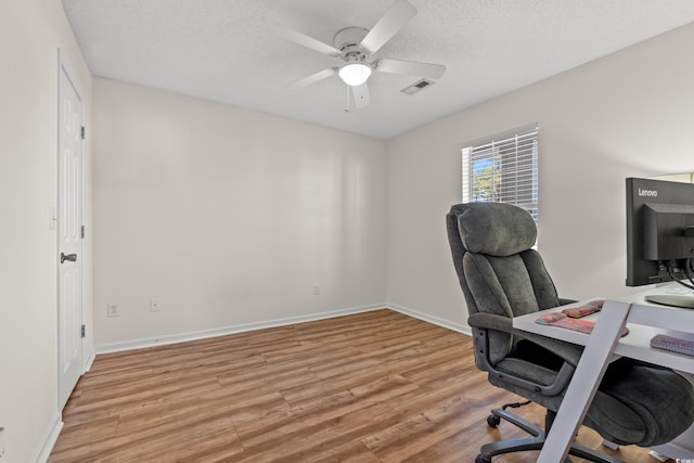 home office featuring a textured ceiling, visible vents, baseboards, a ceiling fan, and light wood-type flooring