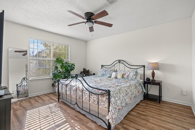 bedroom with a textured ceiling, baseboards, and wood finished floors