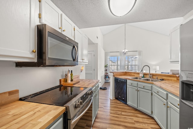 kitchen with decorative light fixtures, wooden counters, appliances with stainless steel finishes, white cabinetry, and a sink