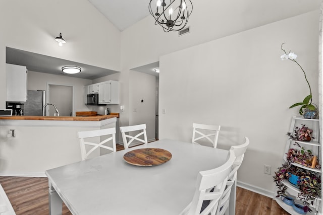 dining area featuring visible vents, a notable chandelier, baseboards, and wood finished floors