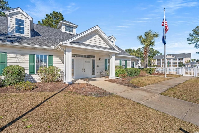 view of front of property with covered porch, a shingled roof, fence, and a front yard