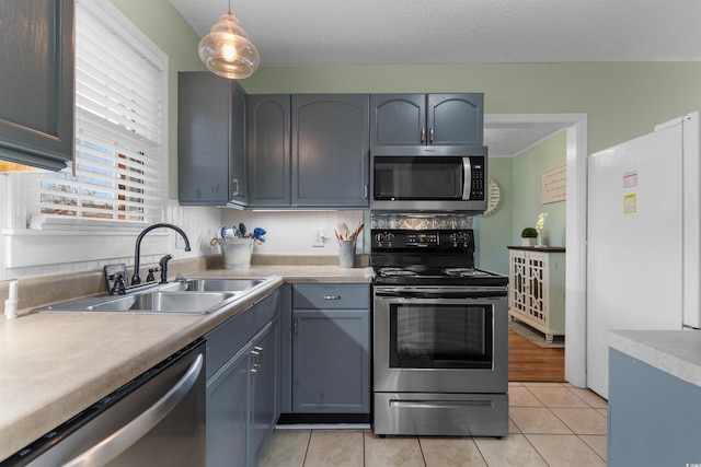 kitchen with a sink, light countertops, light tile patterned floors, decorative light fixtures, and stainless steel appliances