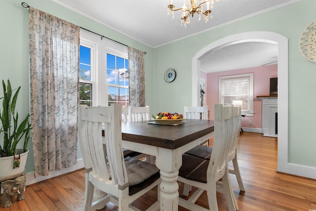 dining room featuring plenty of natural light, light wood-style floors, crown molding, and arched walkways