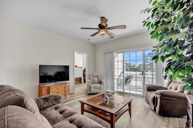 living room featuring visible vents, ceiling fan, light wood-style flooring, and a textured ceiling