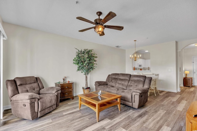 living room featuring light wood-style flooring, baseboards, arched walkways, a textured ceiling, and ceiling fan with notable chandelier